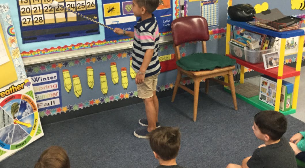 Child pointing at a calendar in a classroom with other children watching