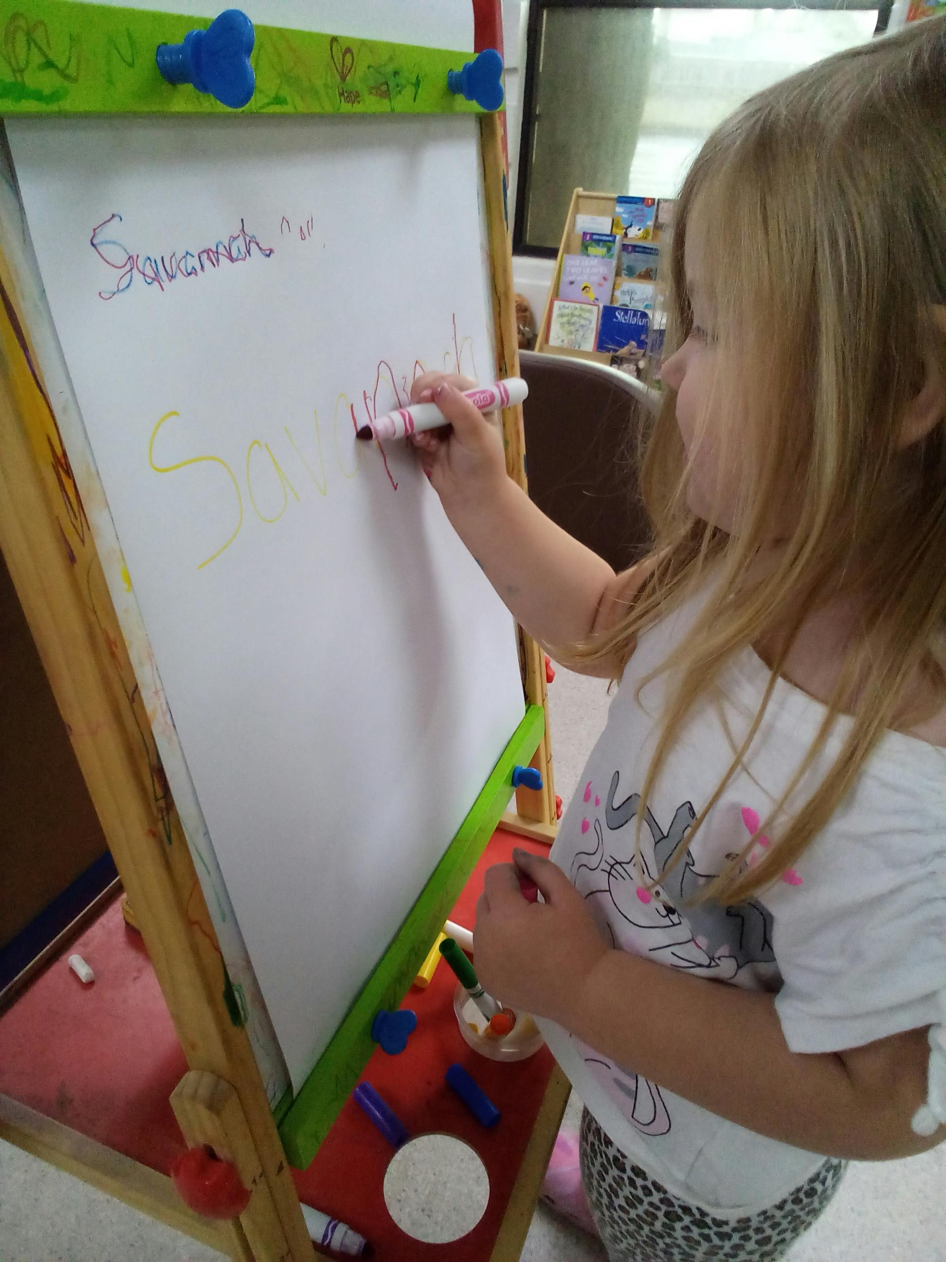 Child writing the name Savannah on a whiteboard