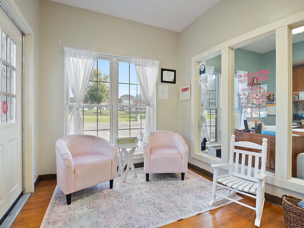 A room with two pink chairs facing a window and a white rocking chair