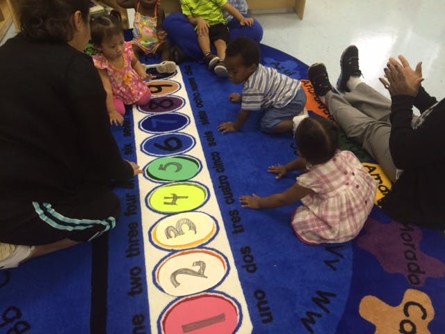 Adults and children on a blue rug with a number line
