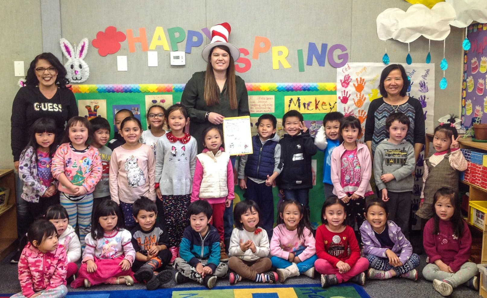 Three adults and many children posing in a classroom