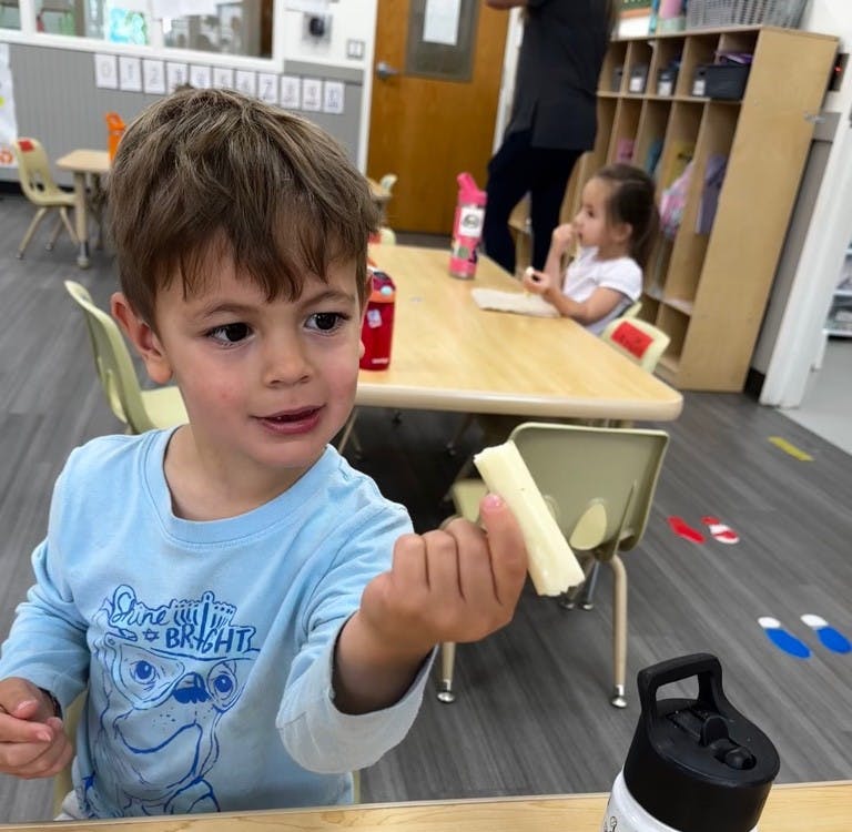 Child holding a piece of cheese in a classroom