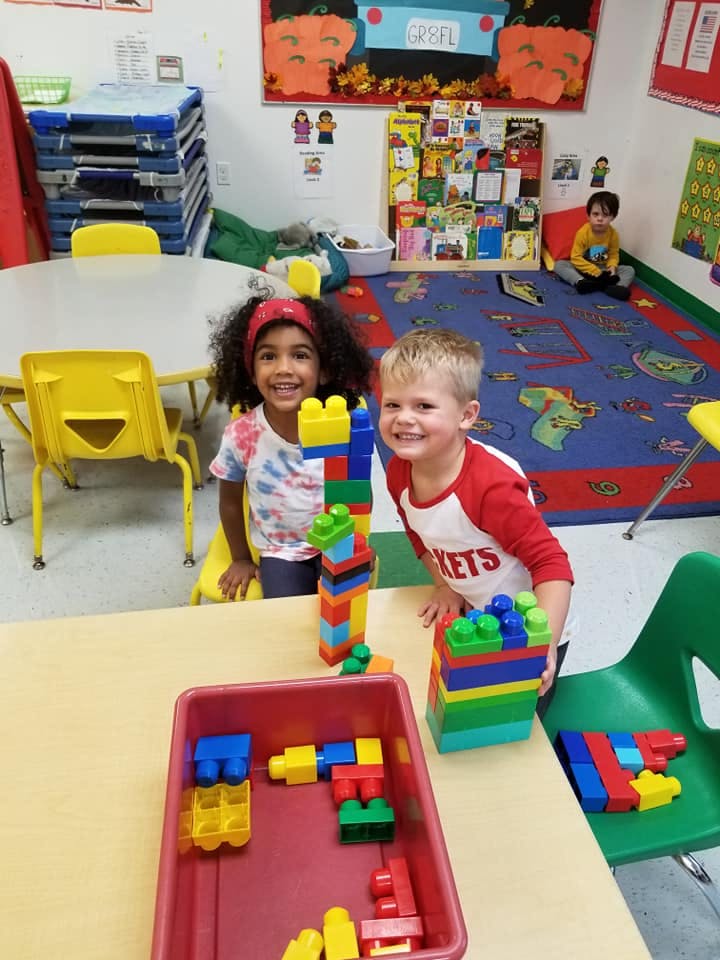 Two children smiling while playing with colorful building blocks in a classroom
