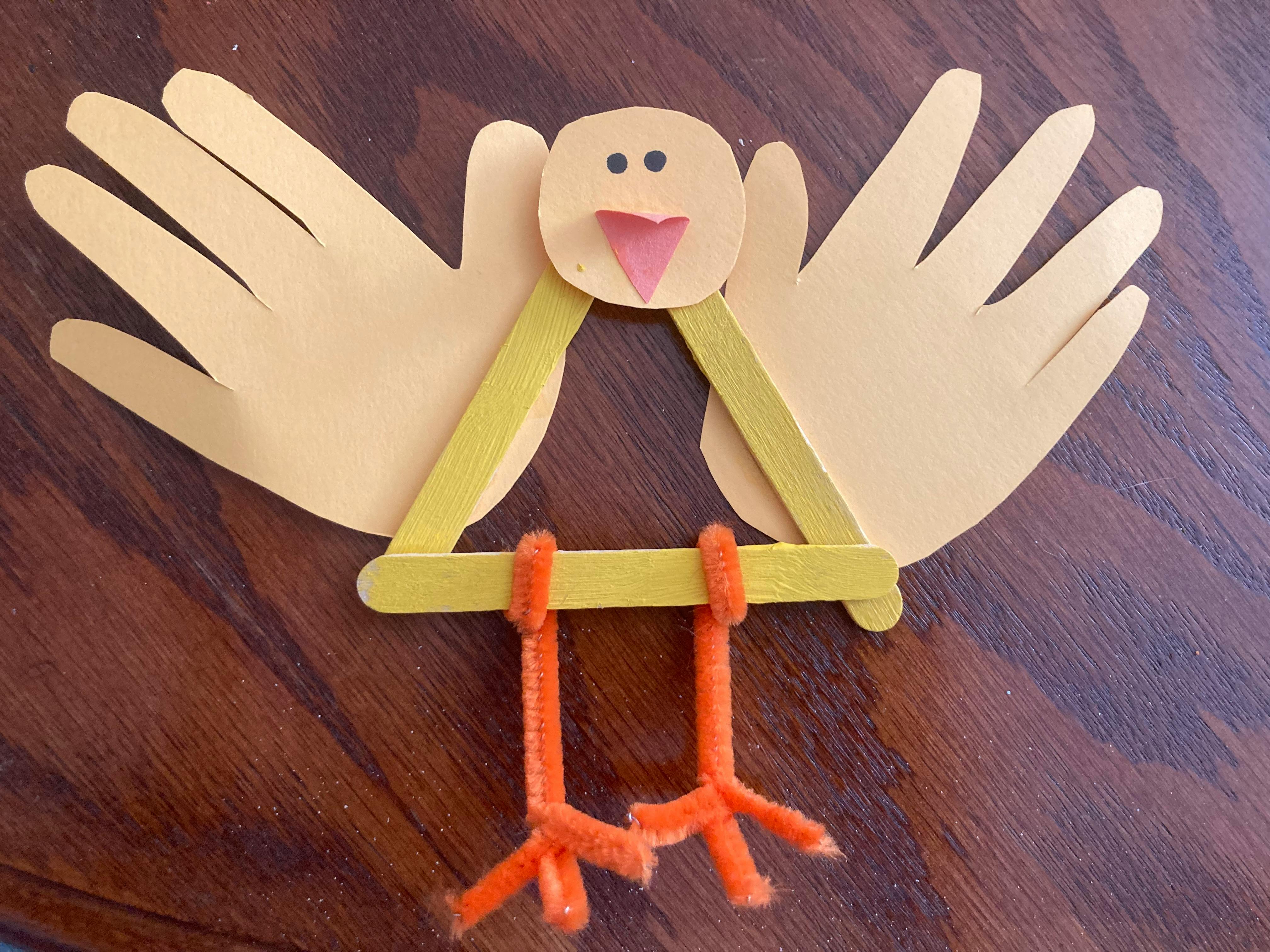 A bird craft made from paper handprints, popsicle sticks, and pipe cleaners
