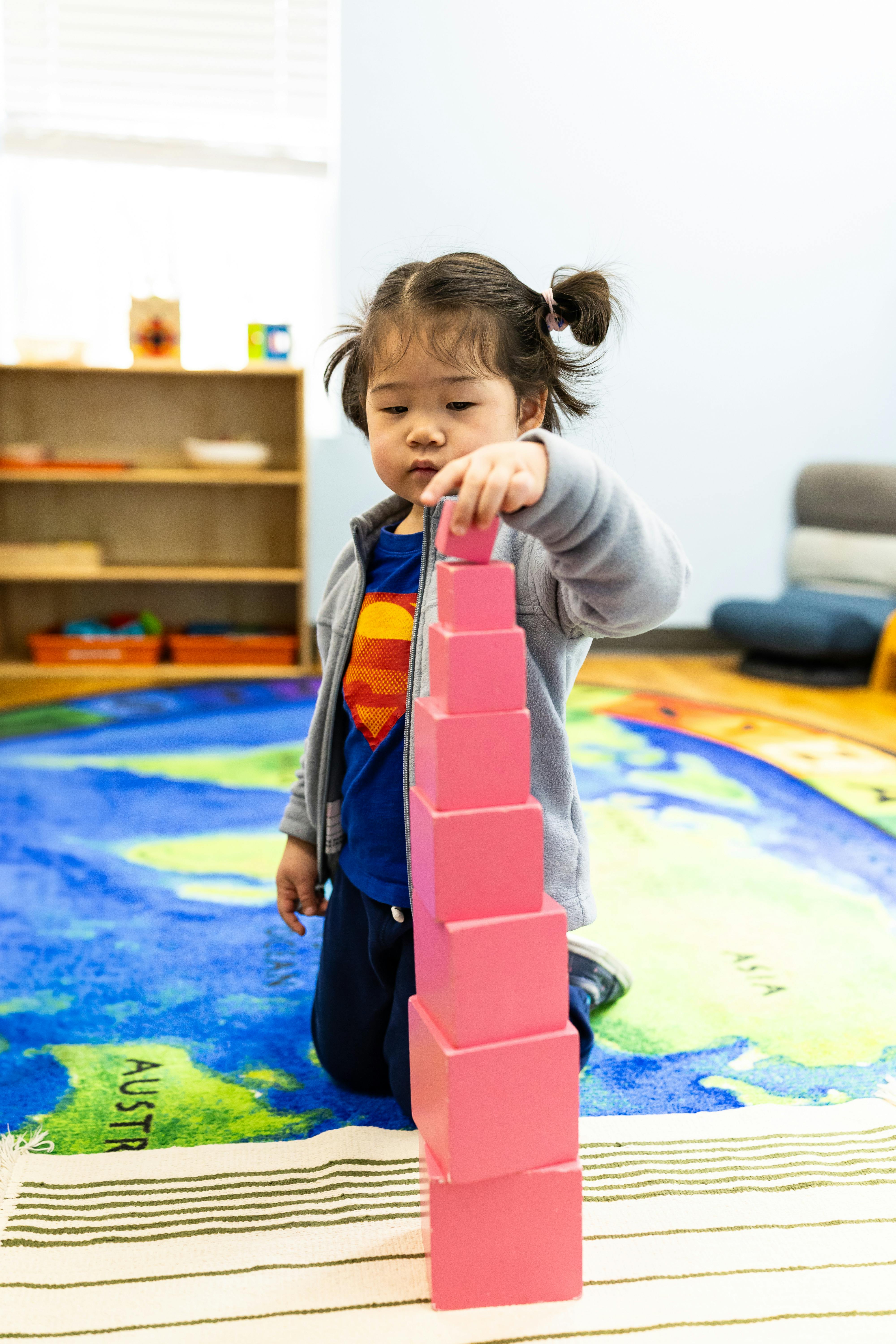 Child kneeling on a map rug, stacking pink blocks