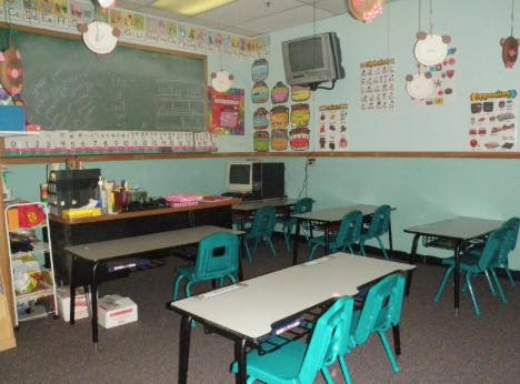 Empty classroom with small desks and chairs, a chalkboard, and wall decorations