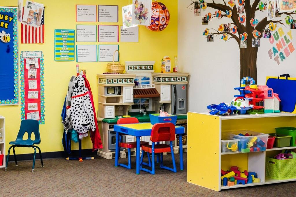 A classroom with a play kitchen, small table and chairs, and toy shelves
