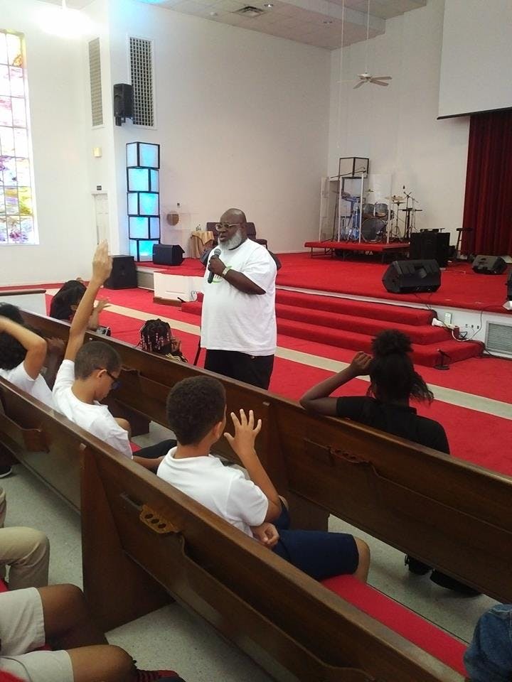 Person speaking into a microphone to children in pews