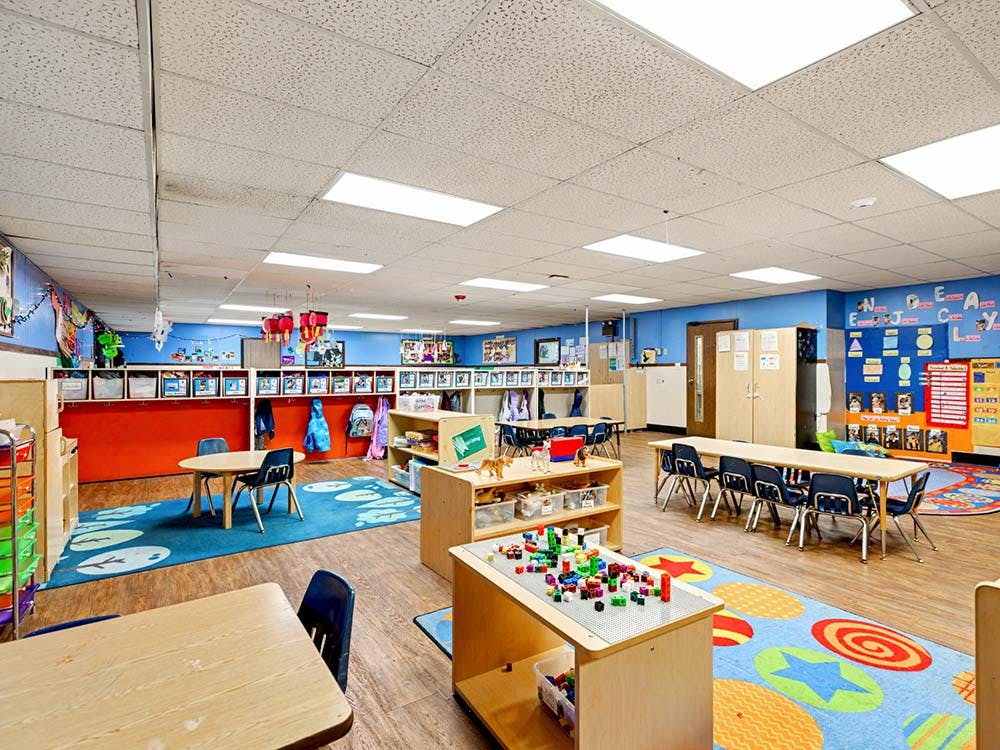 Empty classroom with small tables and chairs, play mats, and learning materials