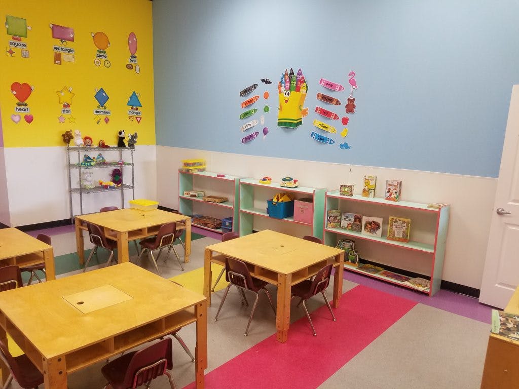 Classroom with small wooden tables and chairs, shelves with toys and books