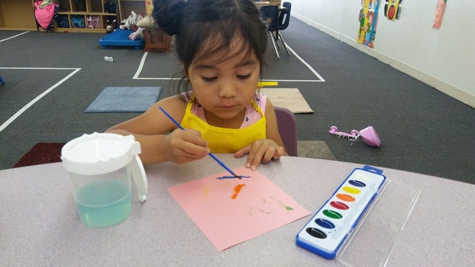 Child painting on paper with watercolors atable and watercolors