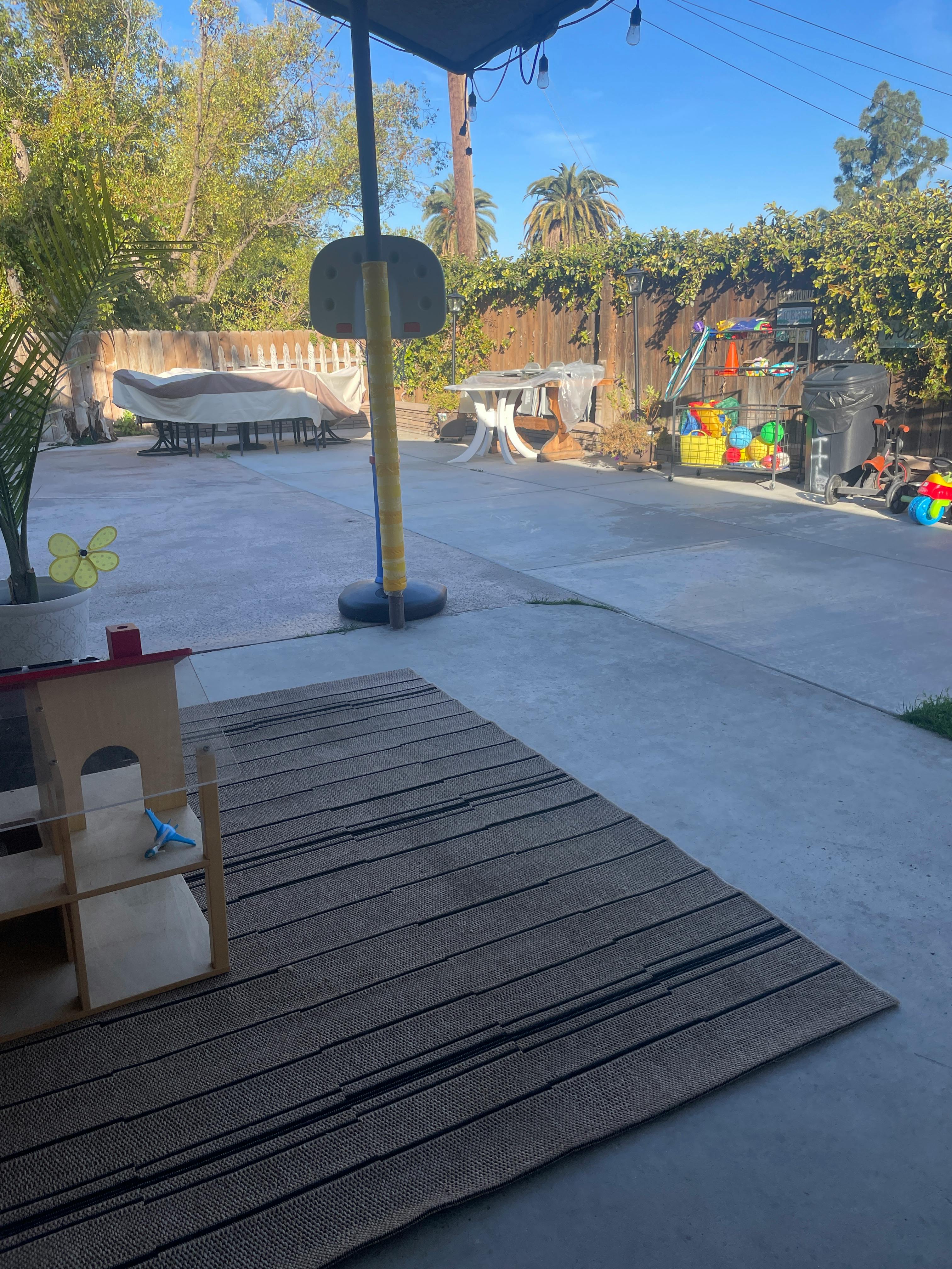 Outdoor patio with a rug, a small wooden structure, and a basketball hoop