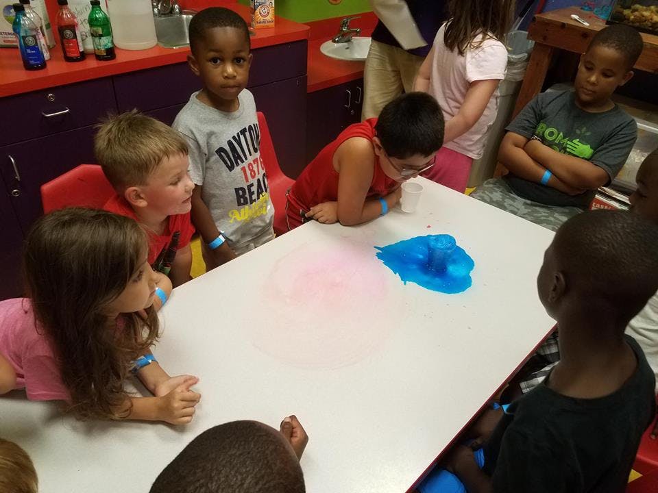 Children gathered around a table with blue and pink substances
