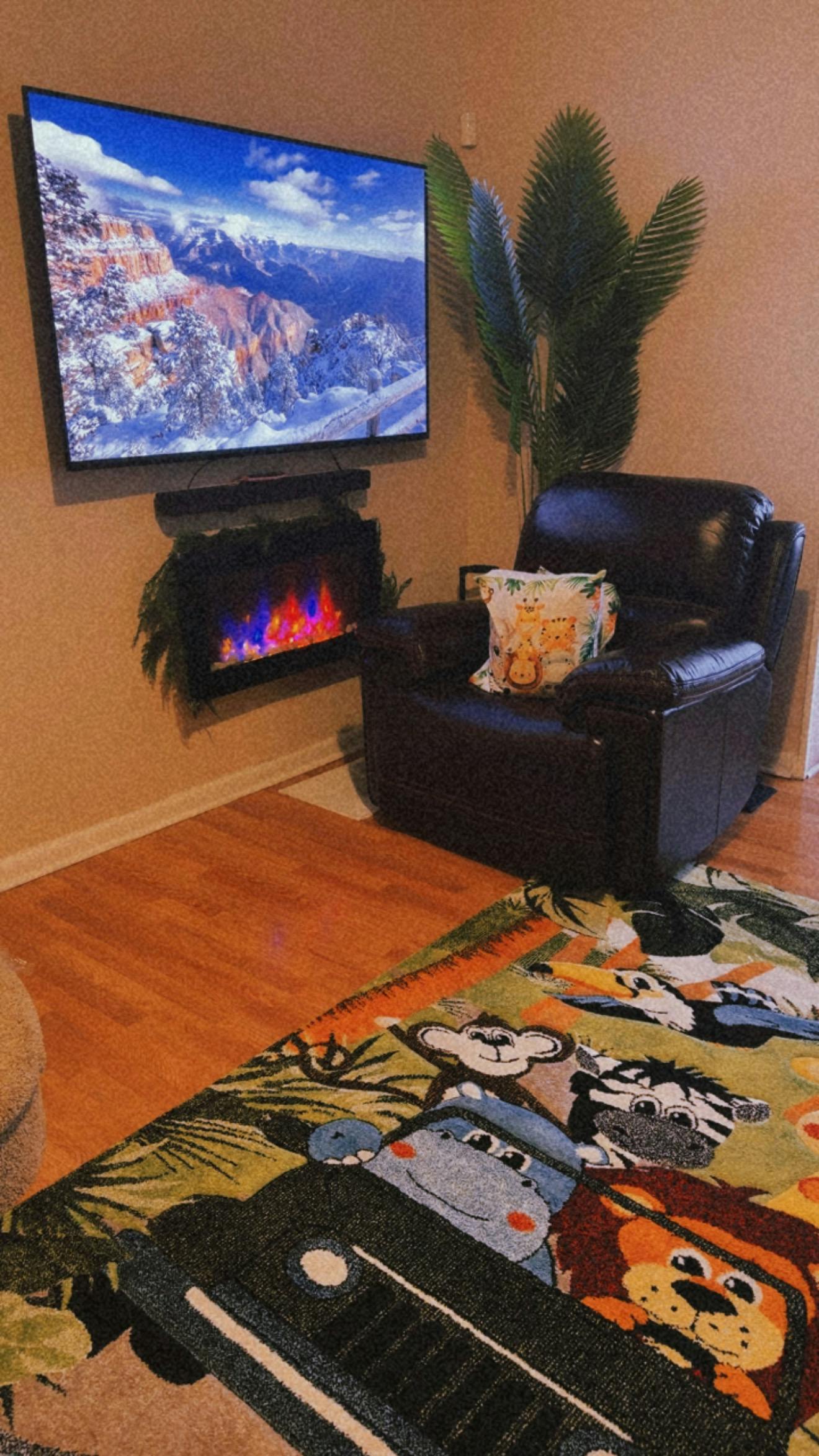 Armchair with a jungle themed rug and a wall mounted television and fireplace