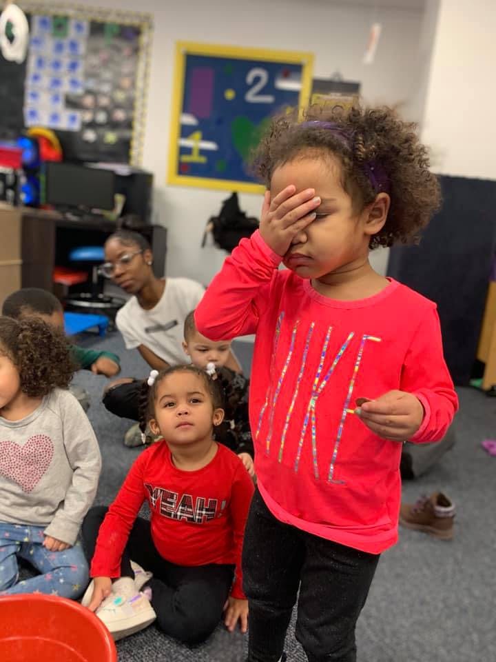 Child covering face with hand in a classroom