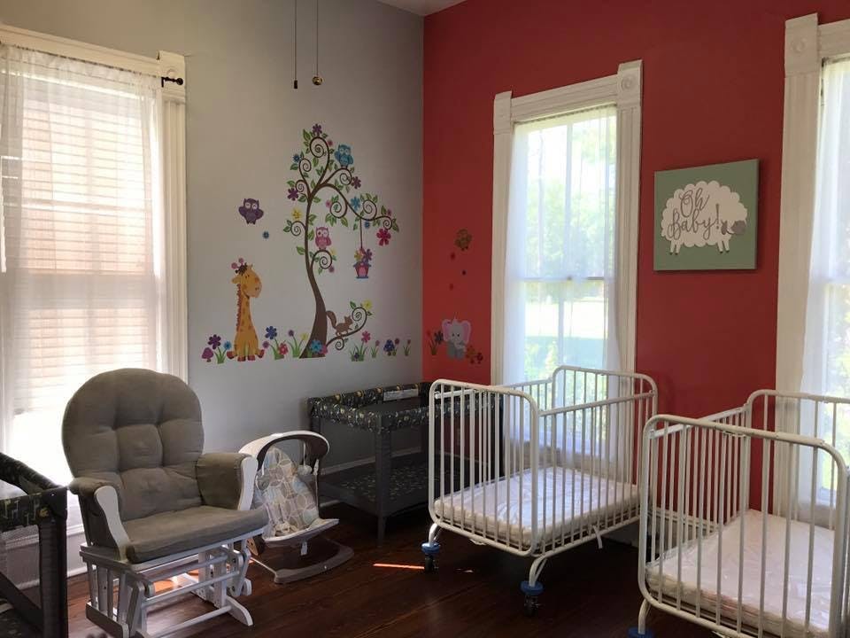 Nursery room with two cribs, a rocking chair, and wall decals