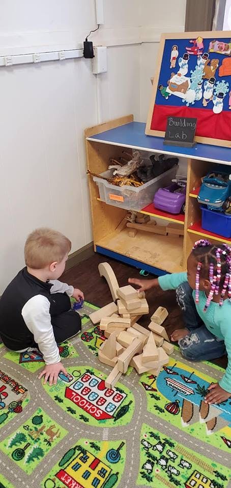 Two children playing with wooden blocks on a rug