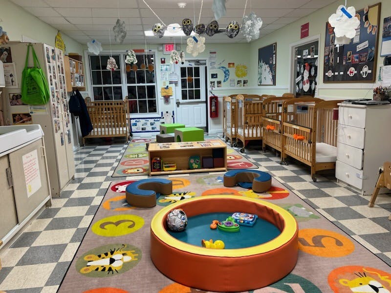 A playroom with multiple cribs, a colorful rug, and various play items