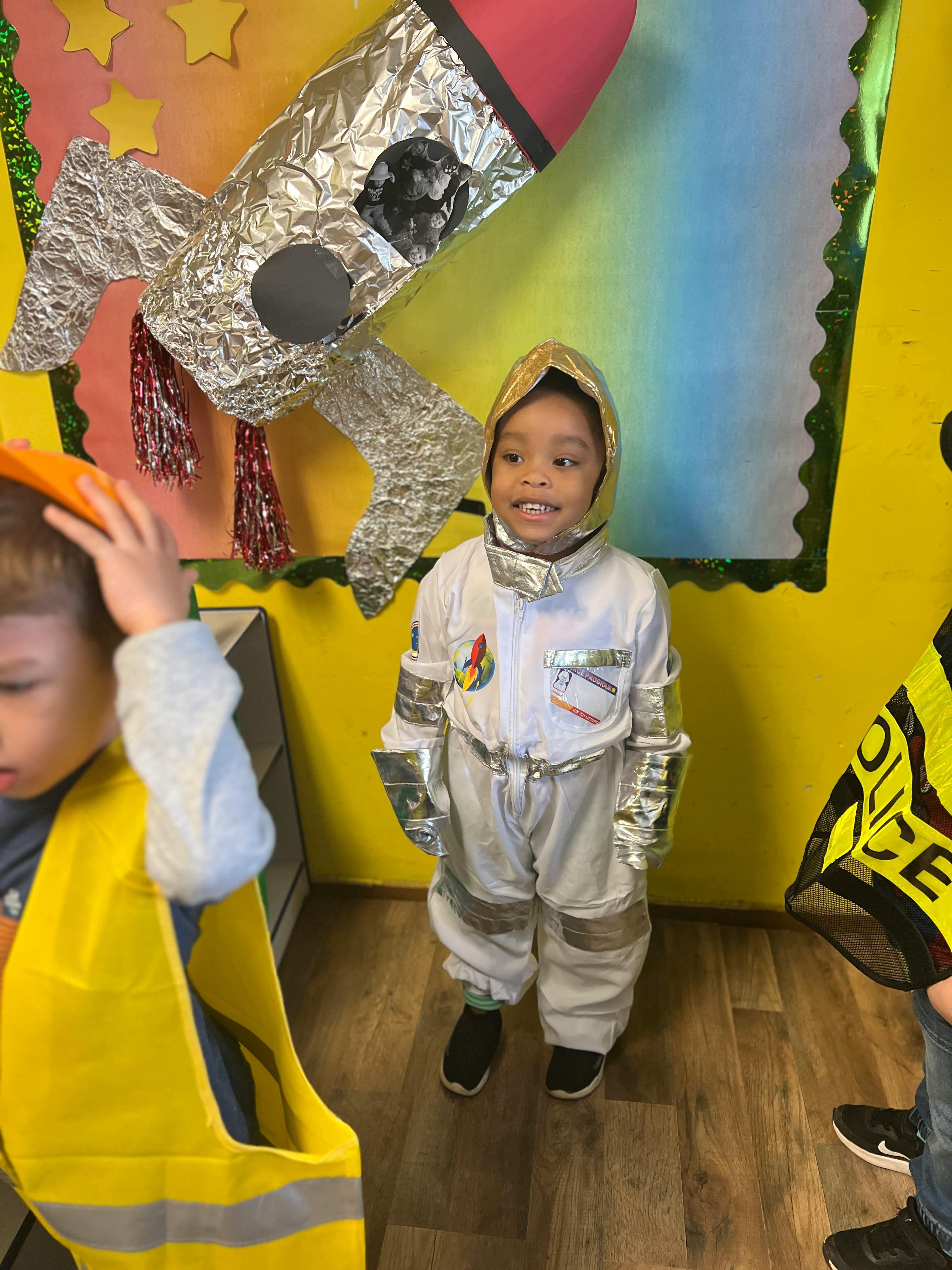Child in an astronaut costume standing next to a rocket decoration