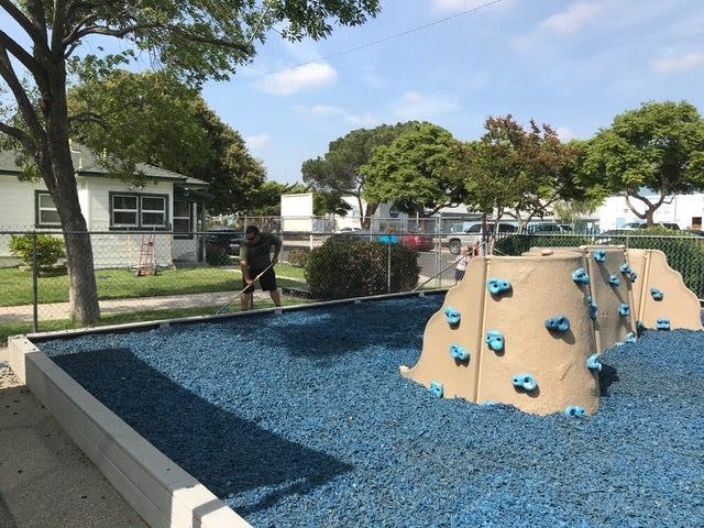 Person raking blue rubber mulch on a playground