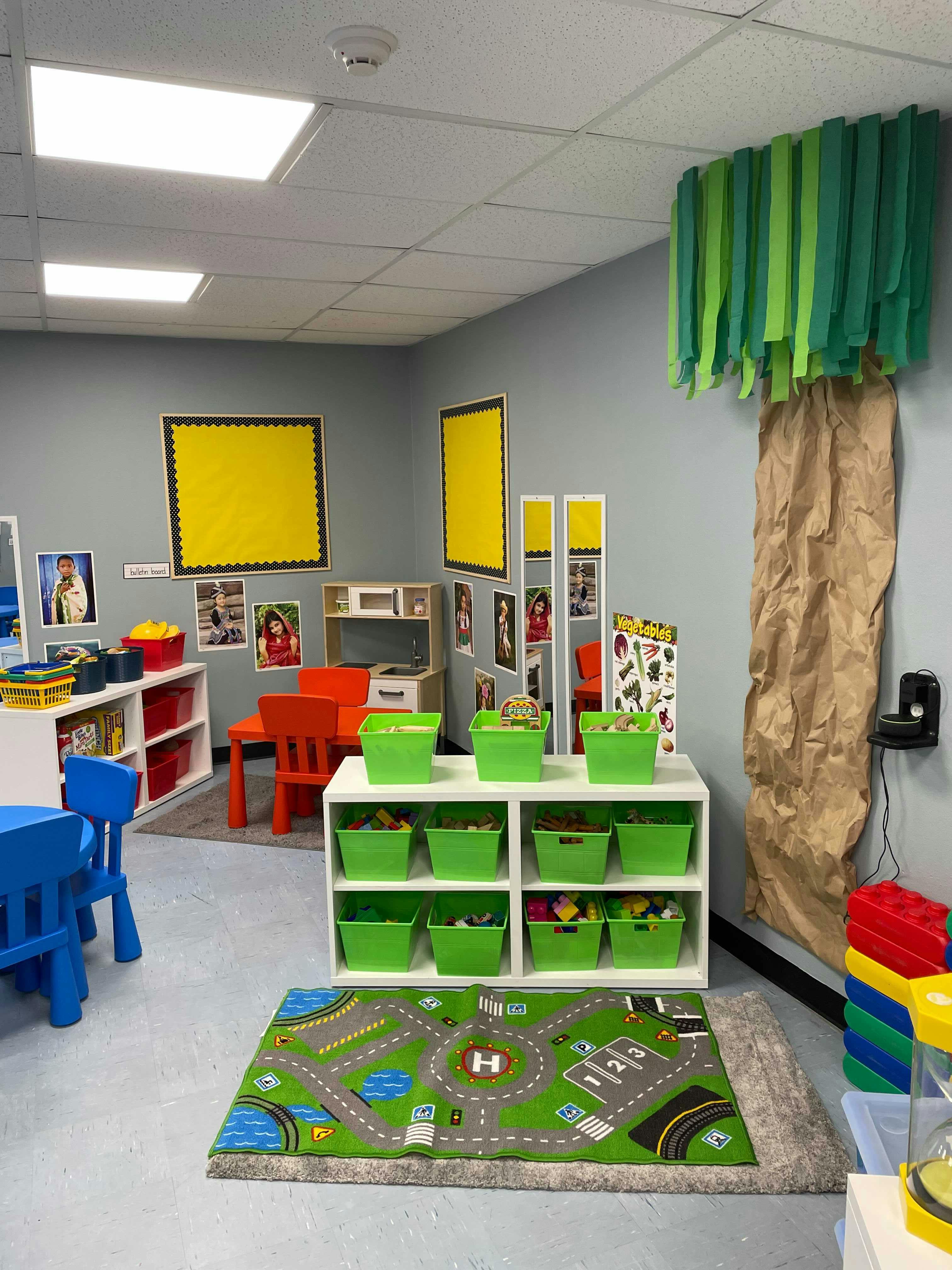 Playroom with small tables and chairs, storage shelves with green bins, and a road map rug