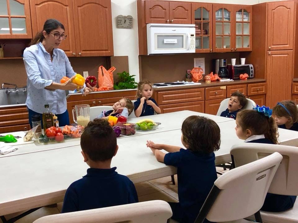 Person holding vegetables in front of children in a kitchen