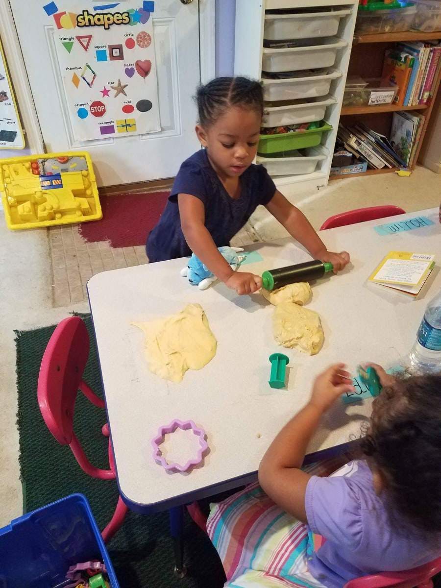 Child rolling playdough with a rolling pin at a table