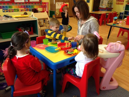 Person and three children playing with toys at a small table in a classroom