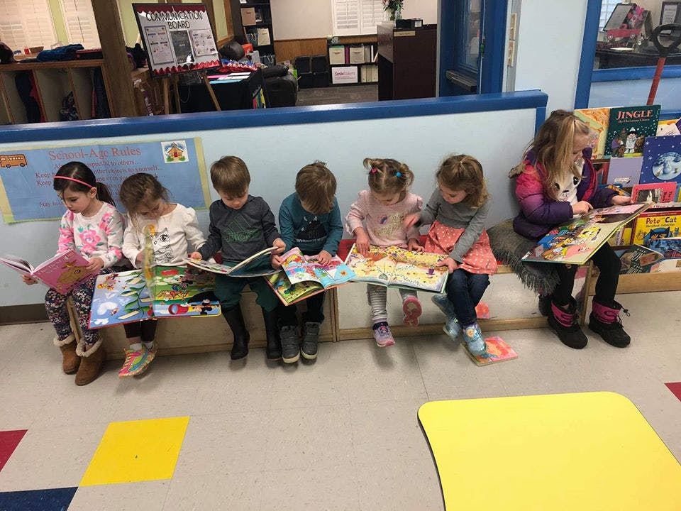 Children sitting on a bench reading books in a classroom