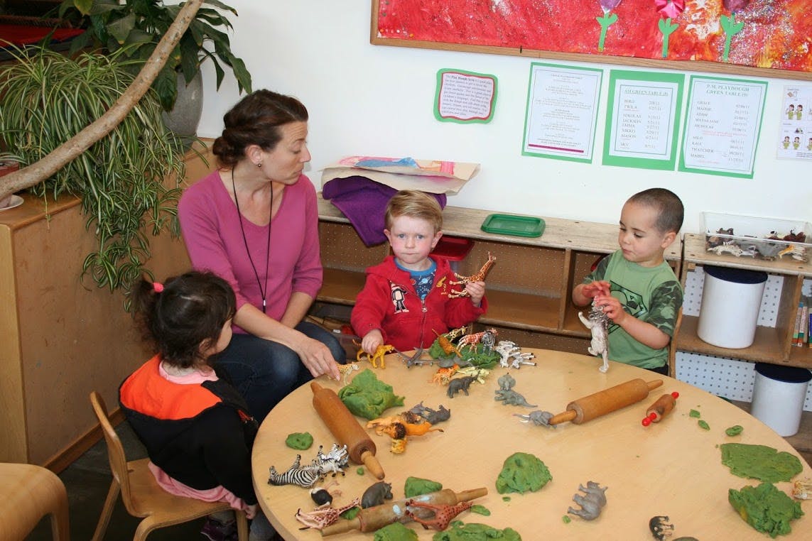 Adult and three children playing with toys and green dough at a table