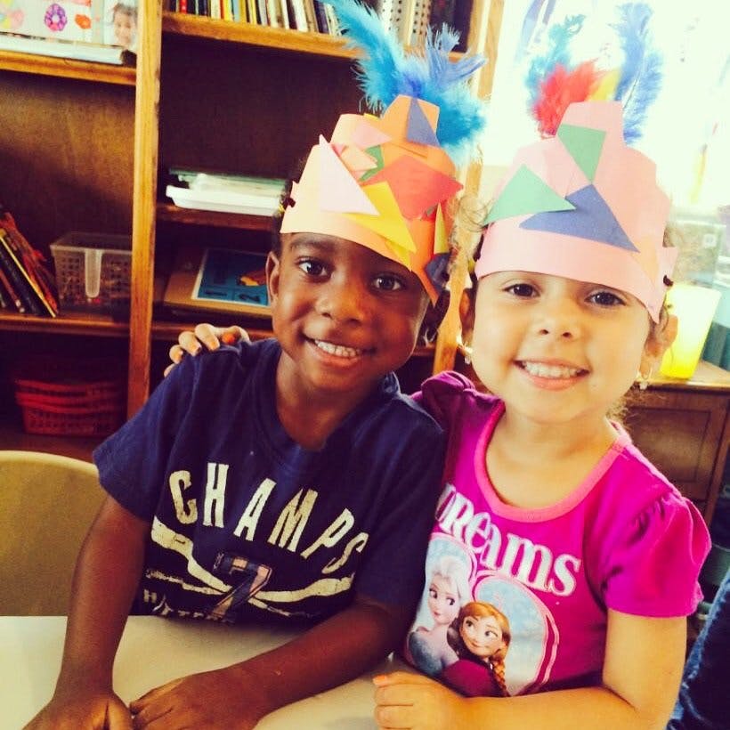 Two children wearing colorful paper crowns with feather hats