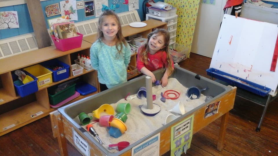 Two children playing at a sand table in a classroom