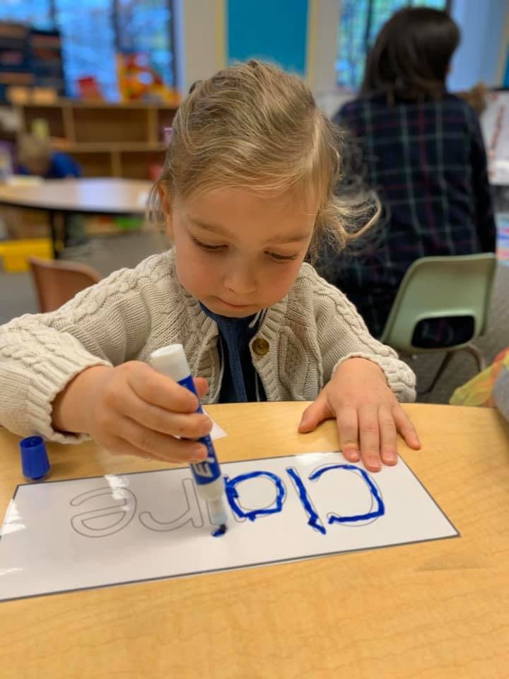 Child tracing letters on paper with a marker in a classroom