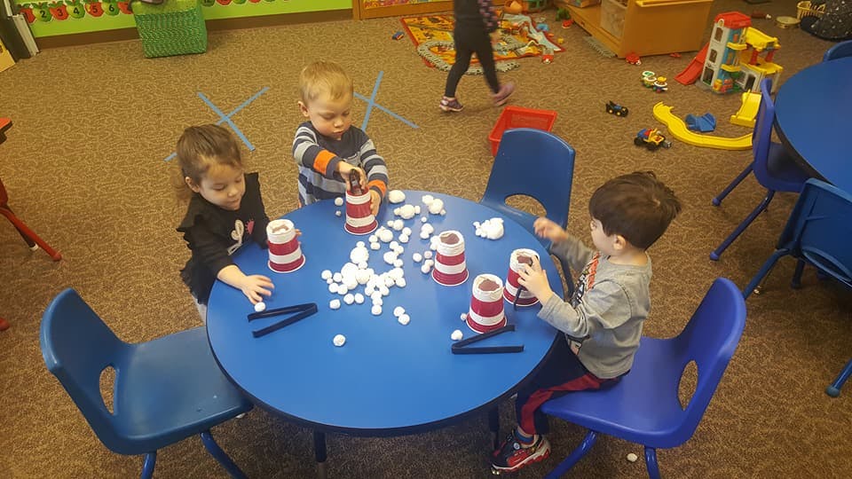 Children playing with cups and small white objects at a blue table