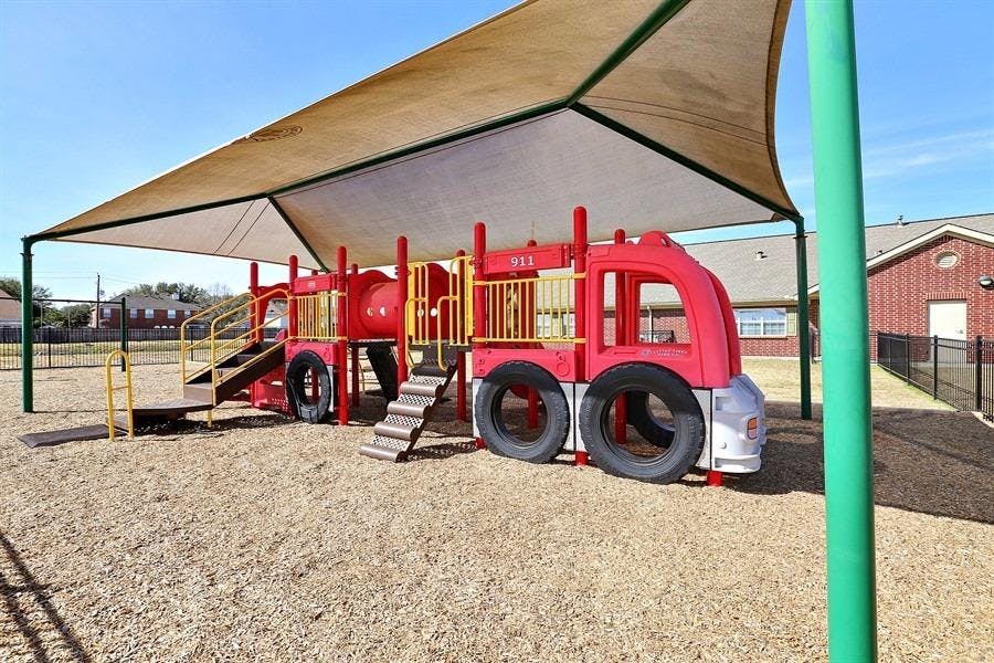Red fire truck-shaped playground equipment under a shade canopy