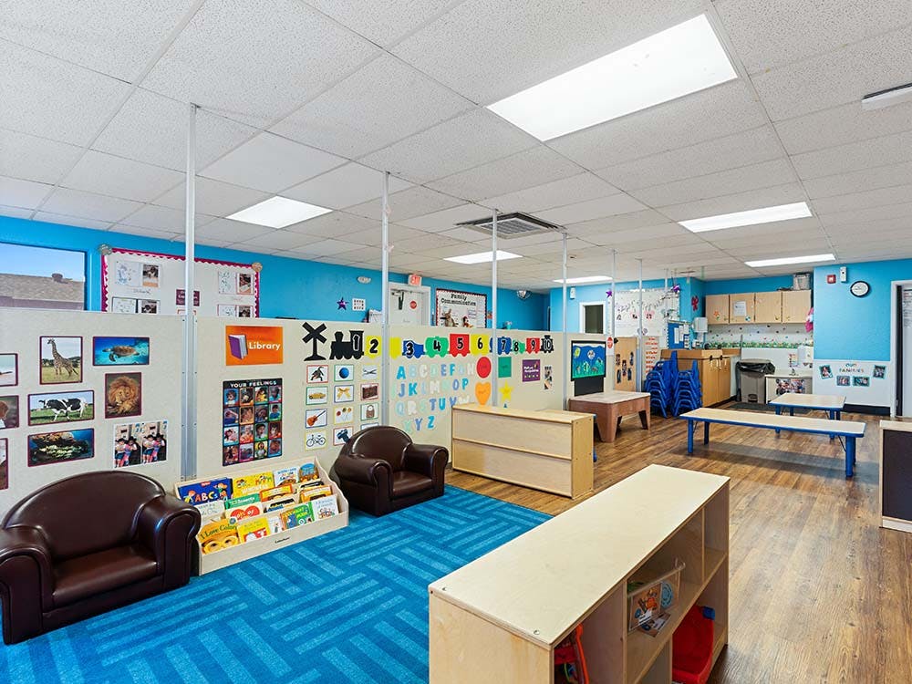 Empty colorful classroom with a blue rug, child-sized furniture, and educational decorations