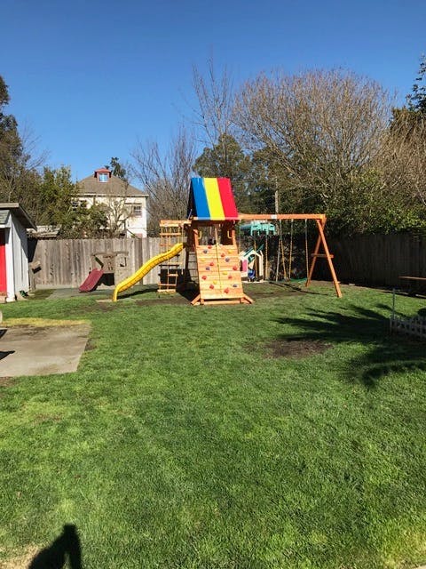 Playground with a slide, climbing wall, and swings in a grassy yard