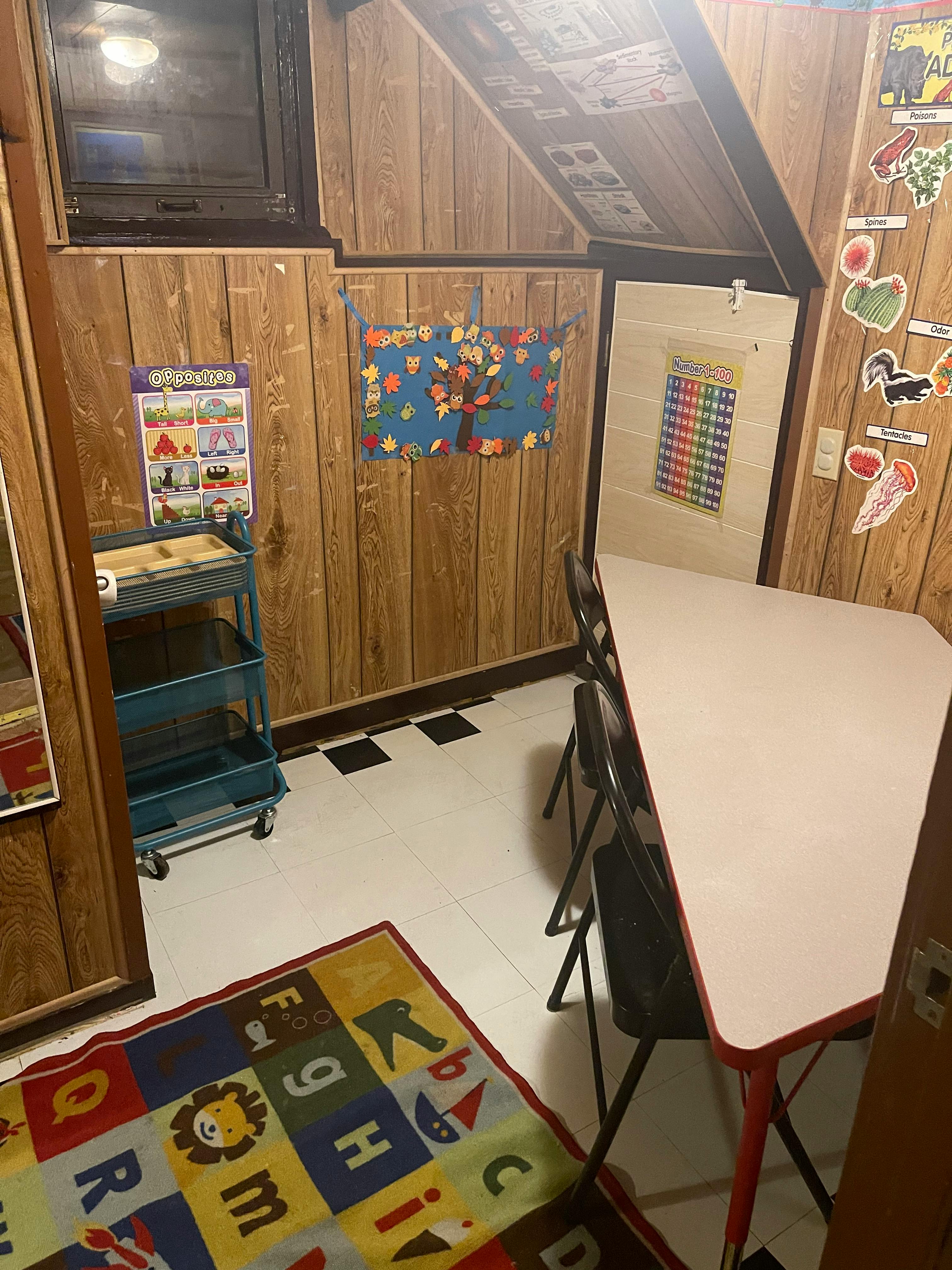 A small room with wood paneling, a table and chairs, and a colorful alphabet rug
