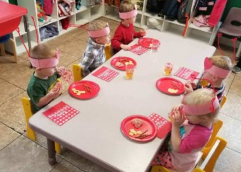 Children with blindfolds sitting at a table with red plates