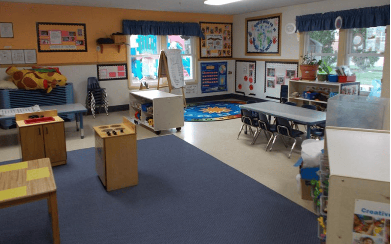 Empty classroom with small tables, chairs, and play equipment