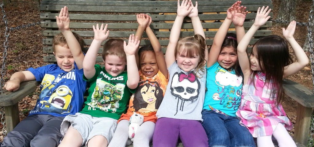 Group of children sitting on a bench with hands raised