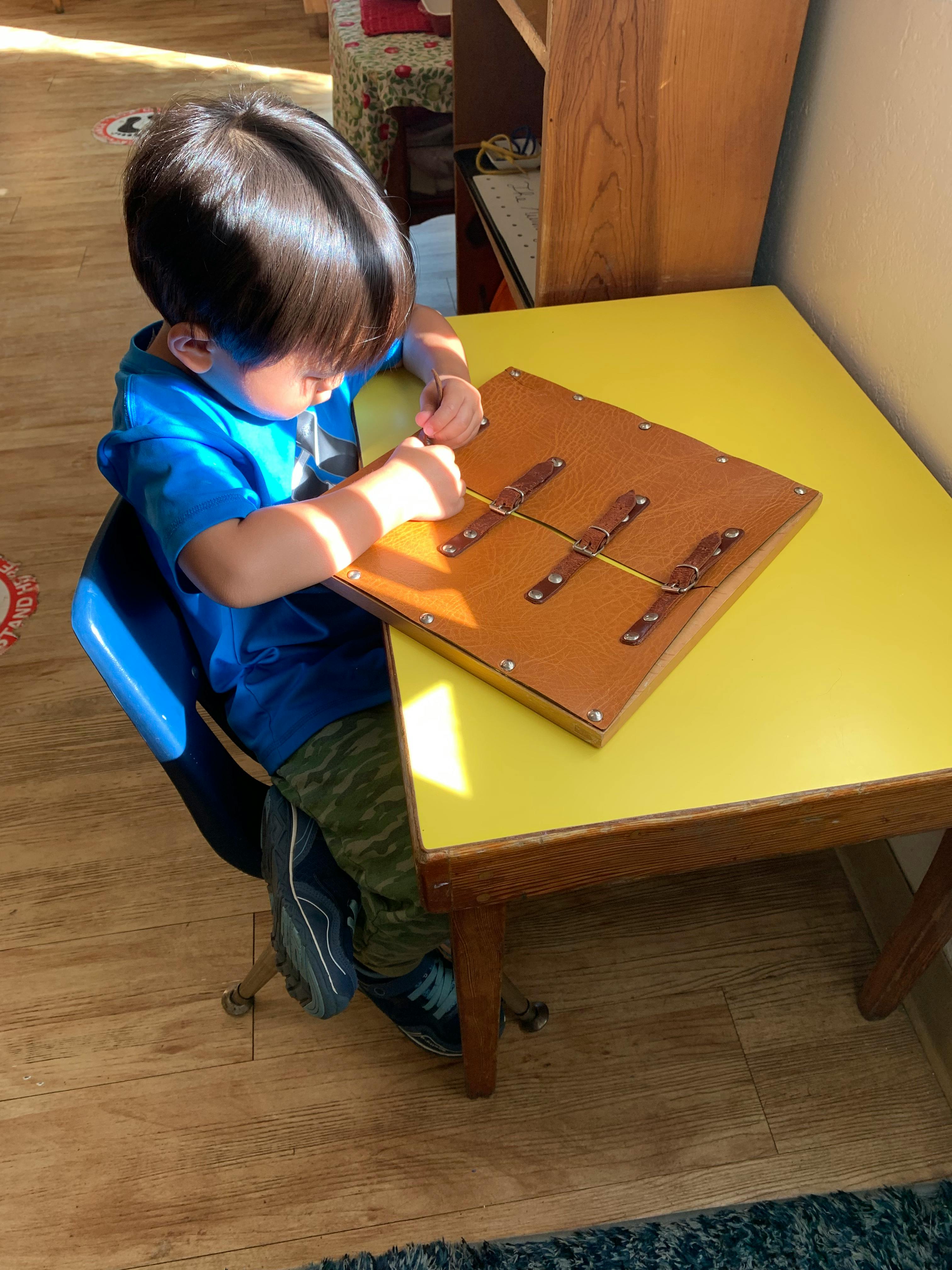 Child playing with a wooden board with elastic bands on a yellow table