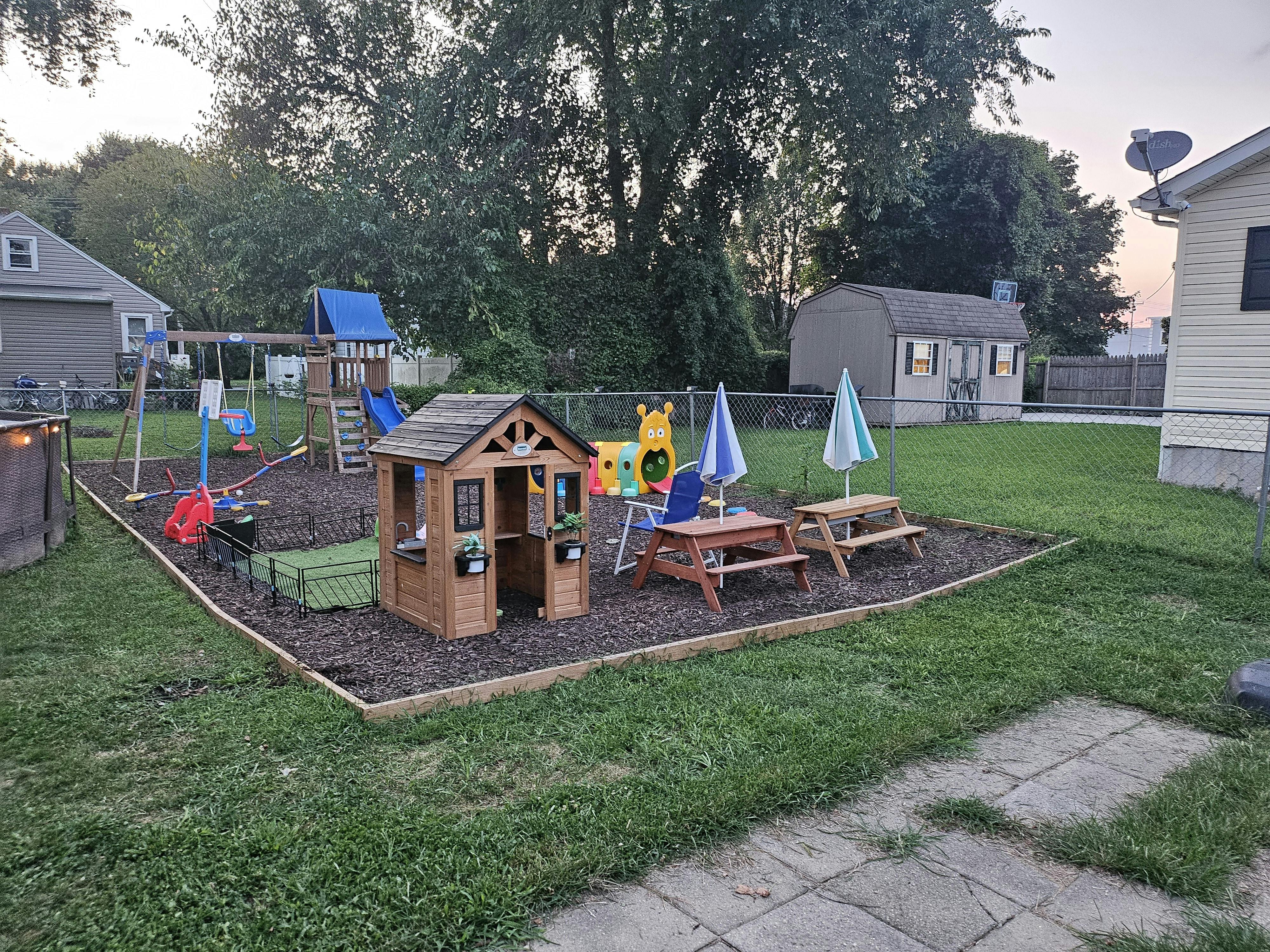 Backyard playground with a wooden playhouse, swings, and picnic tables