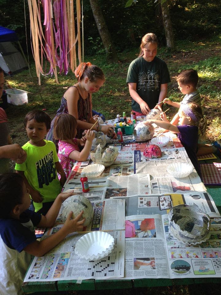 People and children painting paper mache crafts at a table outdoors