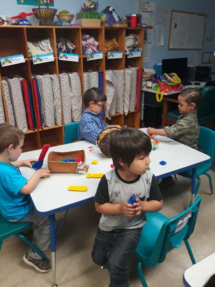 Four children playing with toys at a table in a classroom