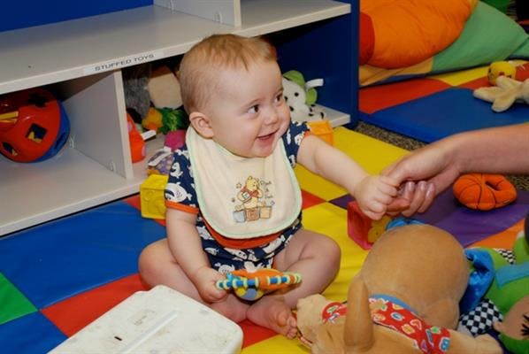 Child in a bib holding a toy and another person's hand