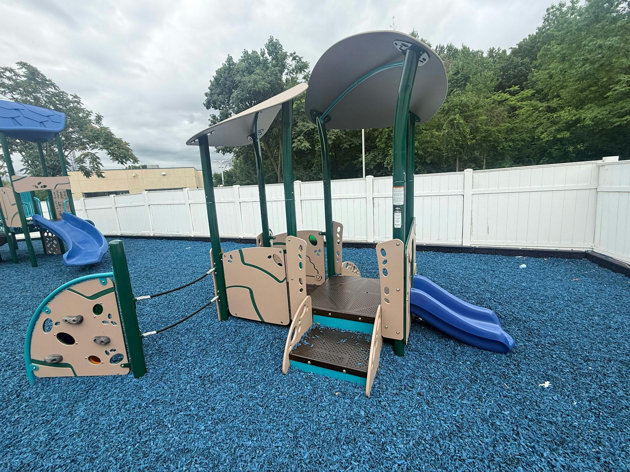 Small playground structure with slides and stairs on blue ground surfacing