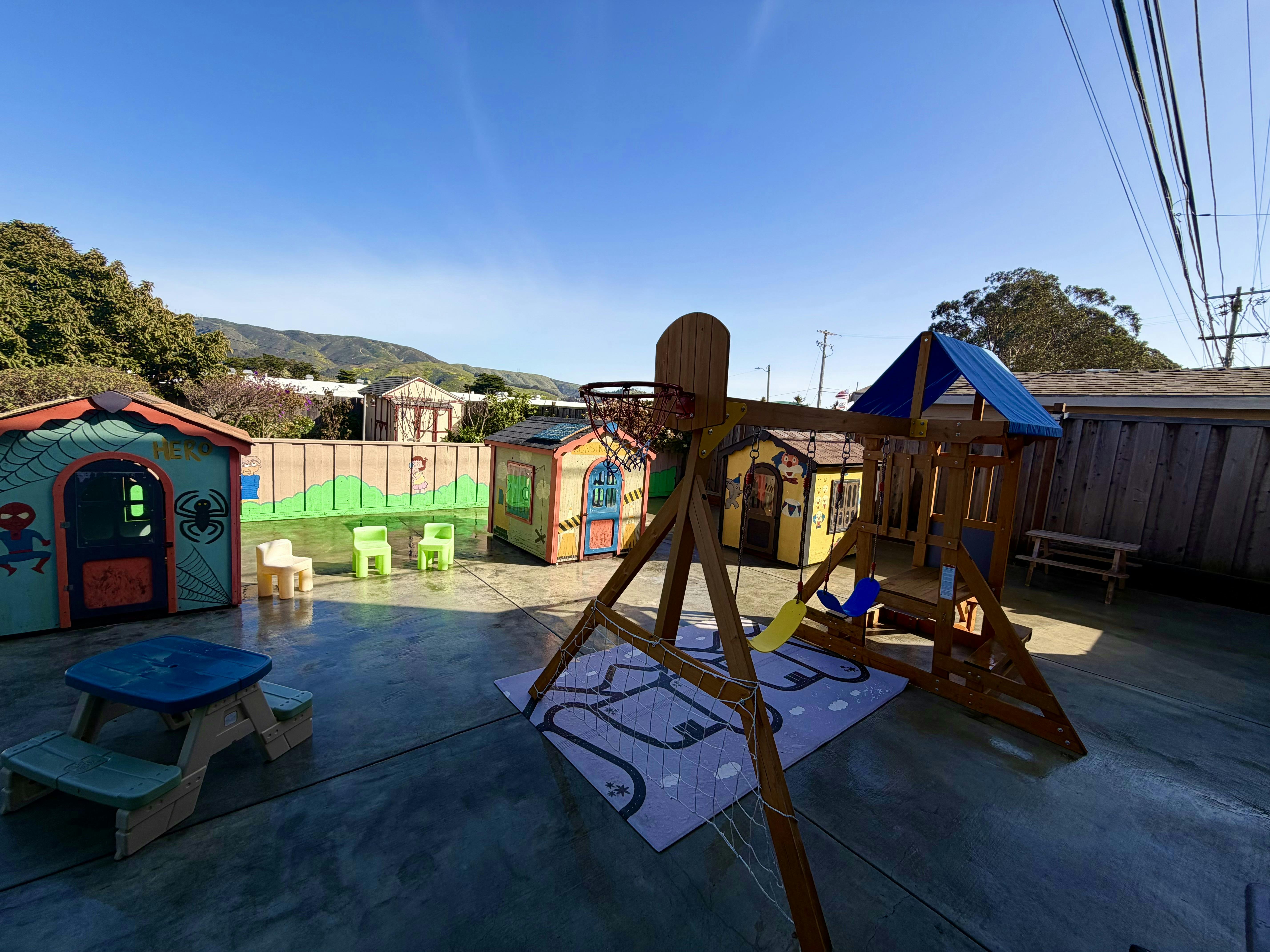 Backyard playground with three playhouses, swings, and a basketball hoop