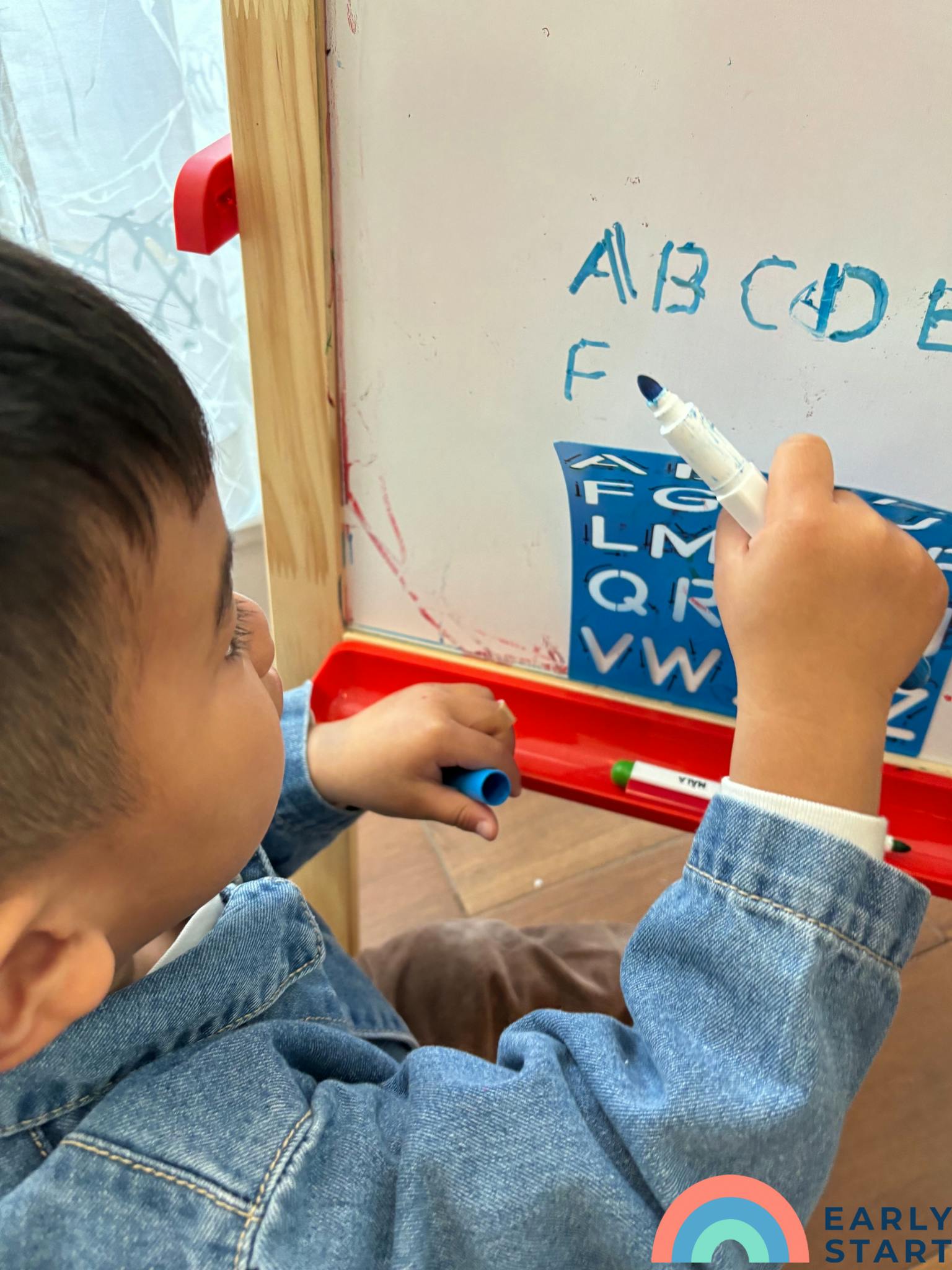 Child writing letters on a whiteboard with a marker