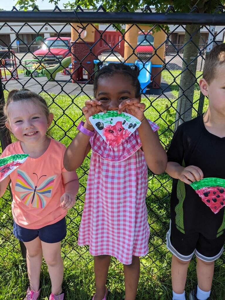 Three children holding up paper watermelon crafts